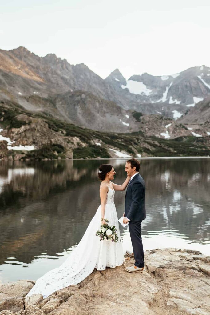 bride and groom in wedding clothes celebrate next to a lake at Colorado mountain elopement