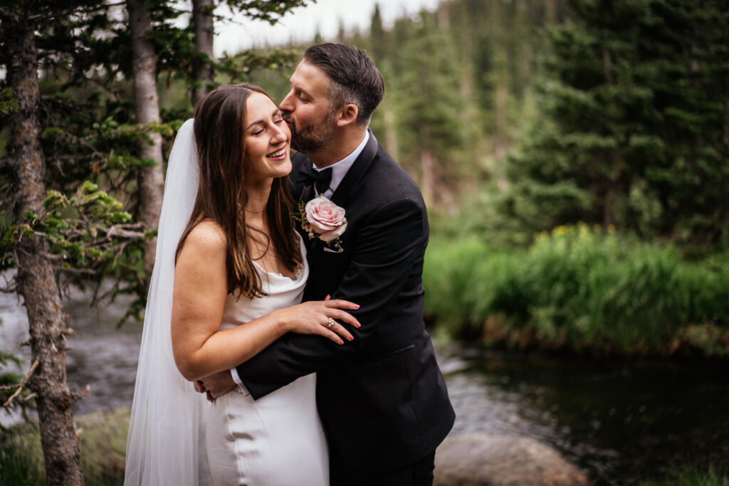 Couple cuddling next to creek in the forest at Boulder, CO elopement.