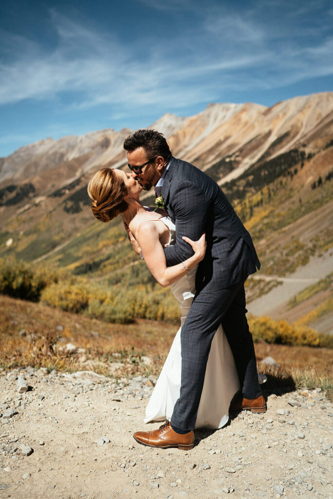 Bride and groom kiss in front of fall colors on Ophir Pass at Telluride, Colorado adventure elopement.