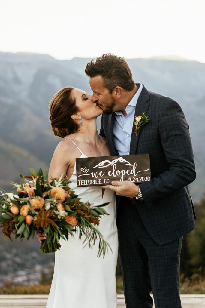 Bride and groom kiss behind "we eloped" sign at Telluride, Colorado elopement.