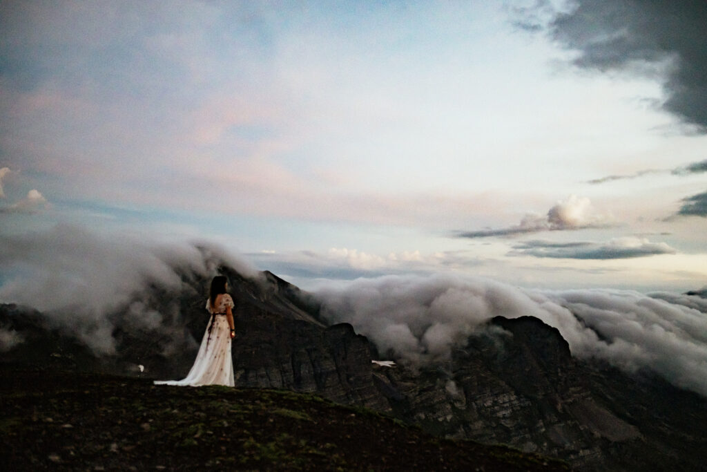 bride in colorful wedding dress stands on top mountain in the clouds at Crested Butte Colorado hiking elopement