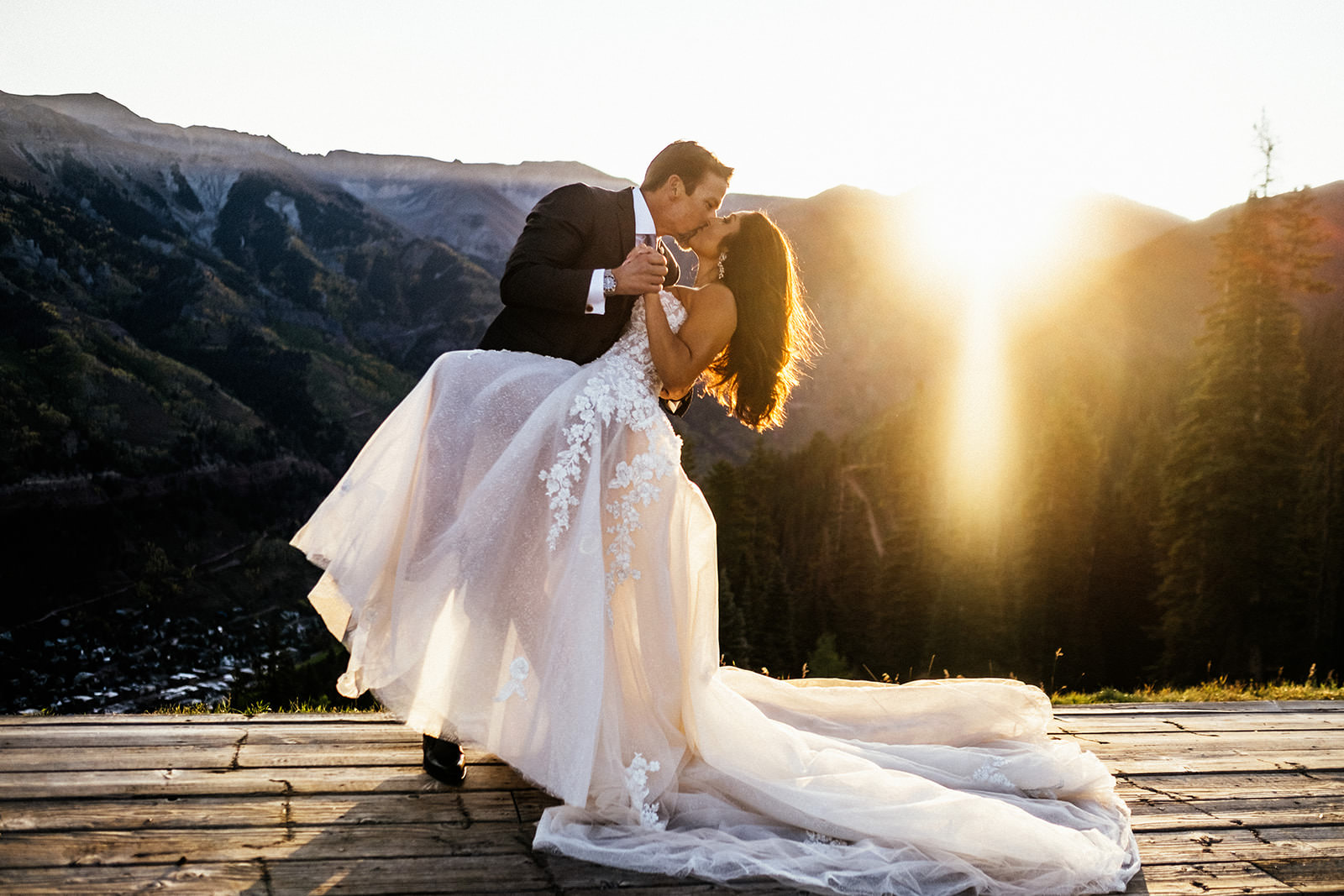 bride and groom kiss on top of mountain as sunlight streams over them at Colorado elopement