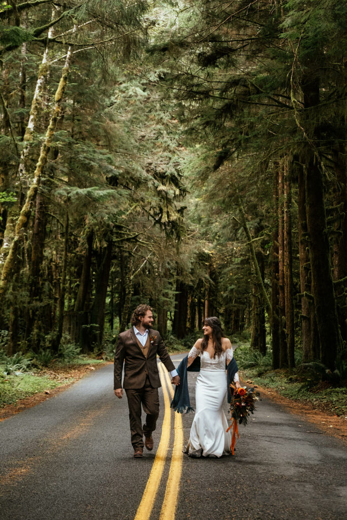 bride and groom hold hands while walking down road at Olympic National Park elopement
